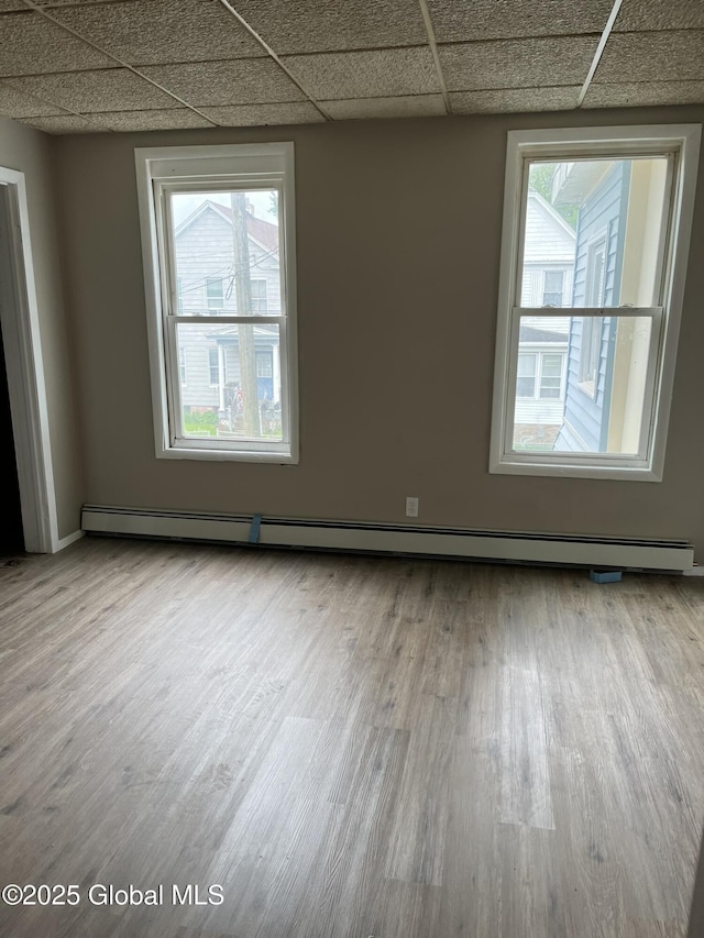 spare room featuring light hardwood / wood-style flooring, a baseboard heating unit, and a paneled ceiling