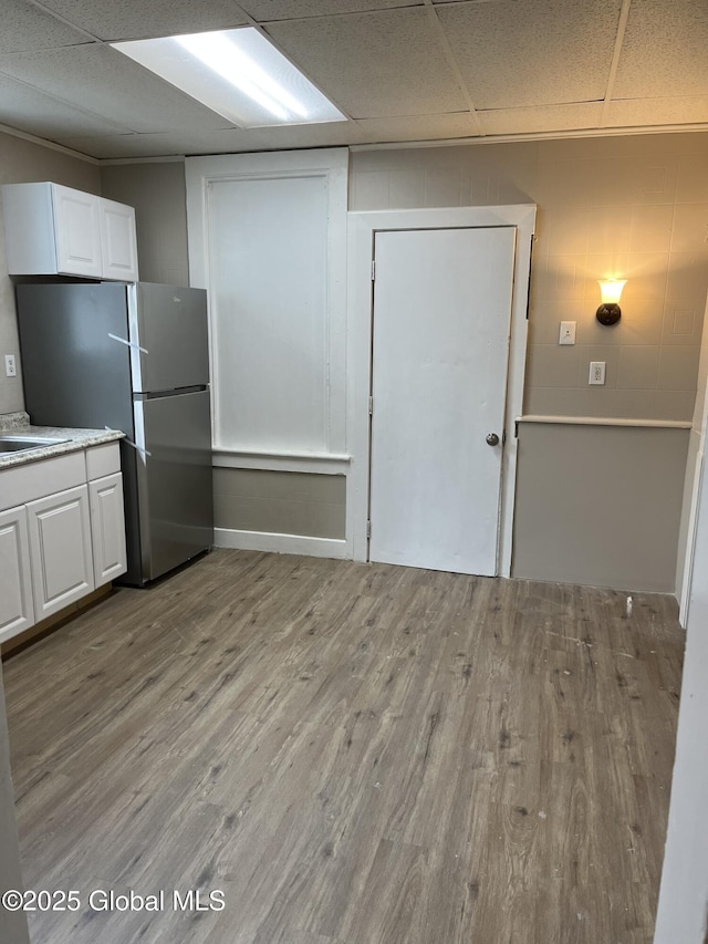 kitchen with light hardwood / wood-style flooring, stainless steel fridge, white cabinets, and a paneled ceiling