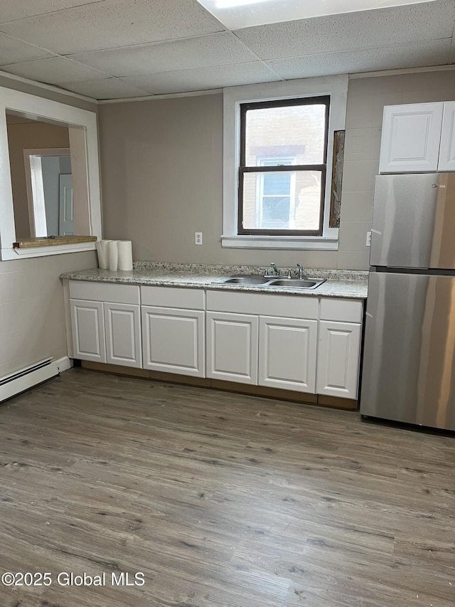 kitchen featuring a paneled ceiling, stainless steel refrigerator, sink, white cabinets, and light wood-type flooring