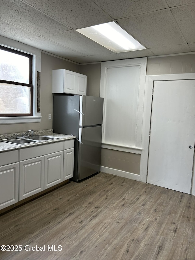 kitchen featuring white cabinetry, stainless steel fridge, light hardwood / wood-style floors, and a drop ceiling