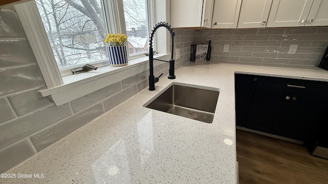 kitchen with white cabinetry, light stone countertops, sink, and backsplash