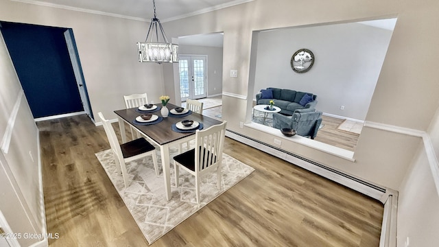 dining space featuring wood-type flooring, ornamental molding, an inviting chandelier, and a baseboard radiator