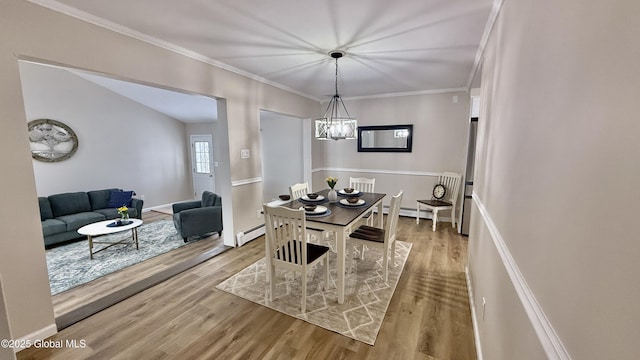 dining space with baseboard heating, wood-type flooring, crown molding, and a notable chandelier