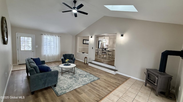 living room with wood-type flooring, lofted ceiling with skylight, ceiling fan, and a wood stove