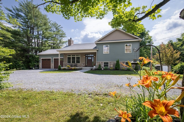 tri-level home with stone siding, gravel driveway, a front yard, a garage, and a chimney