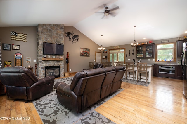 living room featuring a stone fireplace, a healthy amount of sunlight, vaulted ceiling, and light wood finished floors