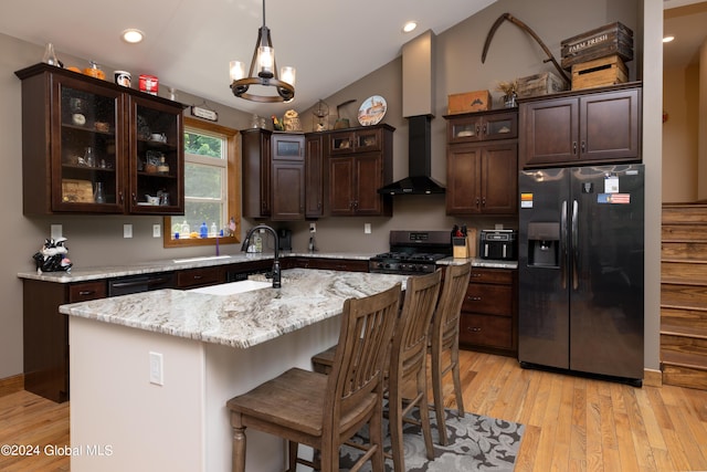 kitchen featuring black appliances, wall chimney range hood, light wood-style flooring, and dark brown cabinetry