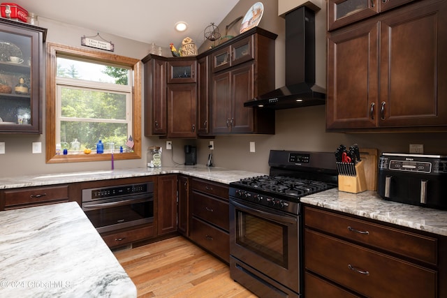 kitchen with dark brown cabinetry, wall chimney range hood, light wood finished floors, and appliances with stainless steel finishes