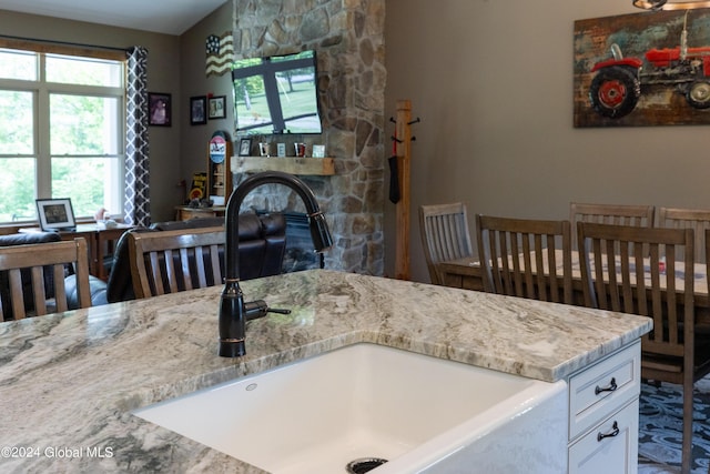 kitchen featuring light stone countertops, a sink, a stone fireplace, white cabinets, and open floor plan