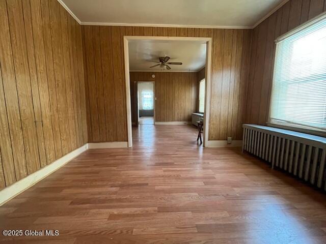 unfurnished room featuring radiator, wood walls, hardwood / wood-style flooring, ornamental molding, and ceiling fan