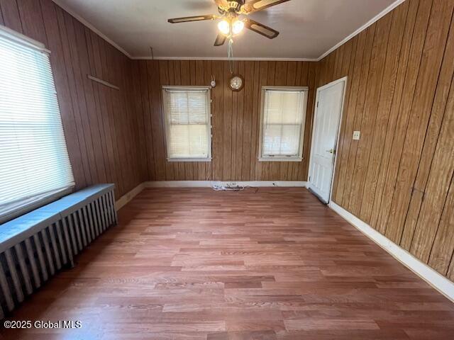 empty room featuring hardwood / wood-style flooring, ornamental molding, radiator, and plenty of natural light