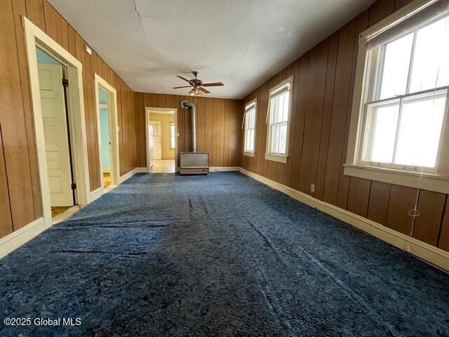 unfurnished living room featuring wooden walls, a wood stove, a healthy amount of sunlight, and carpet