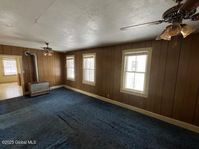 empty room featuring dark colored carpet, wooden walls, a textured ceiling, and ceiling fan