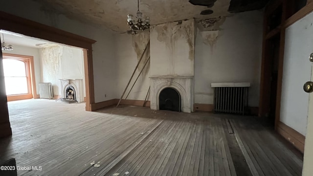 unfurnished living room with an inviting chandelier, radiator heating unit, a fireplace, and wood-type flooring