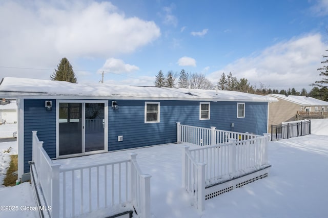 snow covered back of property with a wooden deck