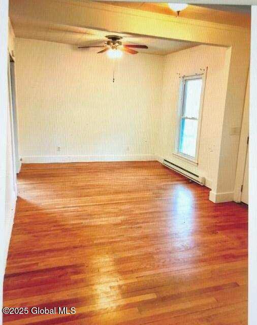 empty room with a baseboard heating unit, hardwood / wood-style flooring, and ceiling fan