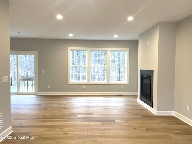 unfurnished living room featuring recessed lighting, baseboards, wood finished floors, and a glass covered fireplace