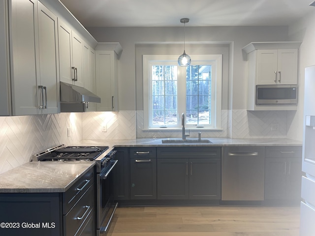 kitchen featuring light wood finished floors, hanging light fixtures, appliances with stainless steel finishes, a sink, and under cabinet range hood