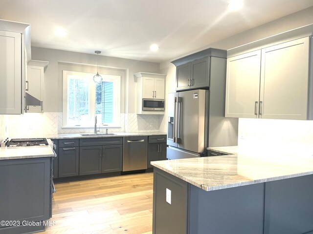 kitchen featuring a peninsula, a sink, light wood-style floors, appliances with stainless steel finishes, and light stone countertops