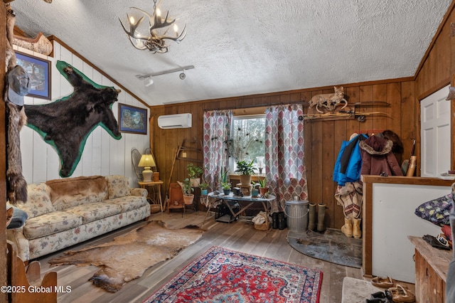 living area featuring an AC wall unit, an inviting chandelier, a textured ceiling, wood walls, and wood-type flooring