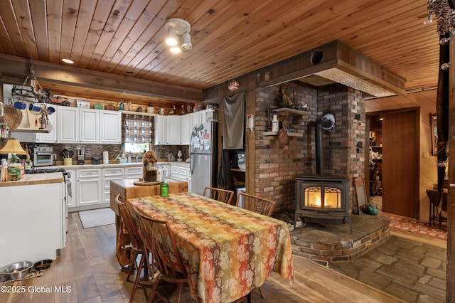 dining space featuring light wood-type flooring, wooden ceiling, a wood stove, and a toaster