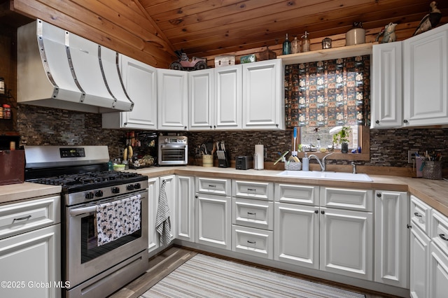 kitchen featuring vaulted ceiling, a sink, white cabinetry, and stainless steel gas range oven