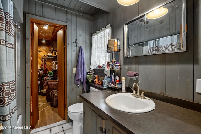 full bath with toilet, tile patterned floors, wooden walls, and vanity