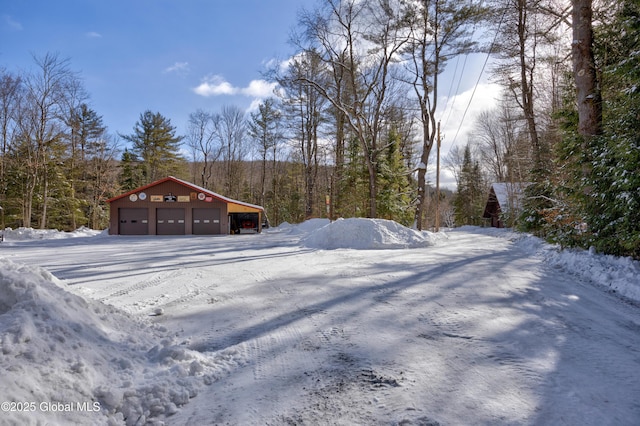 snowy yard featuring an outbuilding, a detached garage, and a forest view
