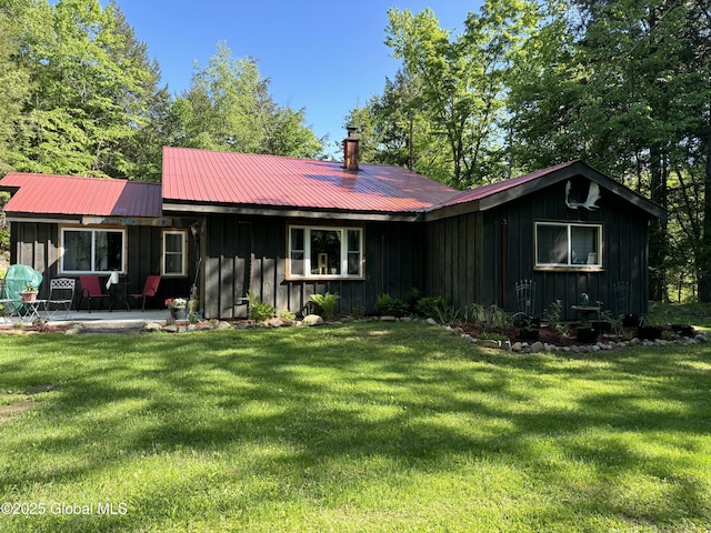 back of house featuring board and batten siding, metal roof, a patio area, and a lawn