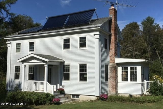 back of property with solar panels and a porch