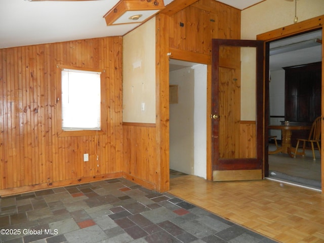 spare room with vaulted ceiling, dark parquet floors, and wood walls