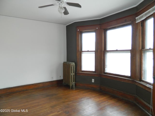 empty room featuring radiator, dark wood-type flooring, a healthy amount of sunlight, and ceiling fan