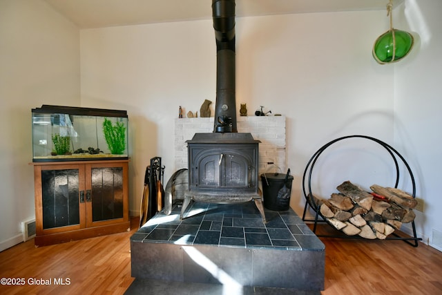 interior details with a wood stove, wood finished floors, visible vents, and baseboards