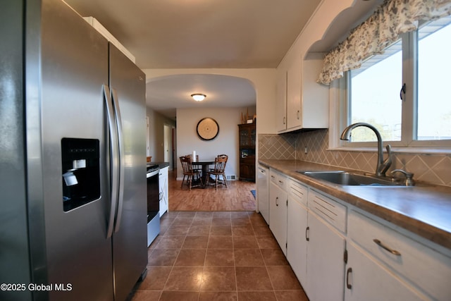 kitchen with arched walkways, a sink, appliances with stainless steel finishes, white cabinetry, and tasteful backsplash