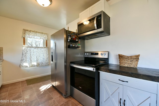 kitchen with tile patterned flooring, appliances with stainless steel finishes, white cabinetry, and baseboards