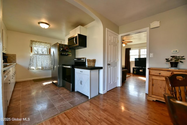 kitchen featuring dark countertops, arched walkways, white cabinets, electric stove, and stainless steel microwave