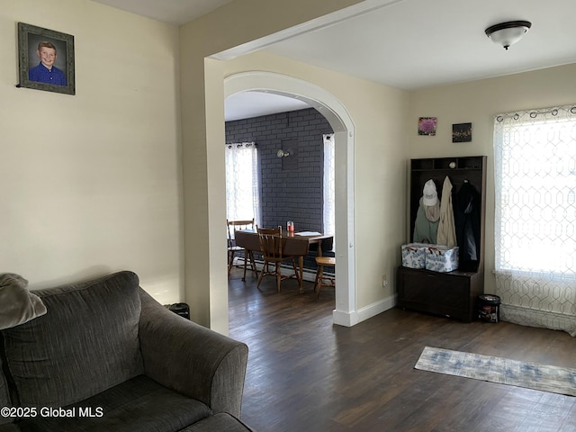 living area featuring dark wood-style floors, a baseboard heating unit, arched walkways, and a wealth of natural light