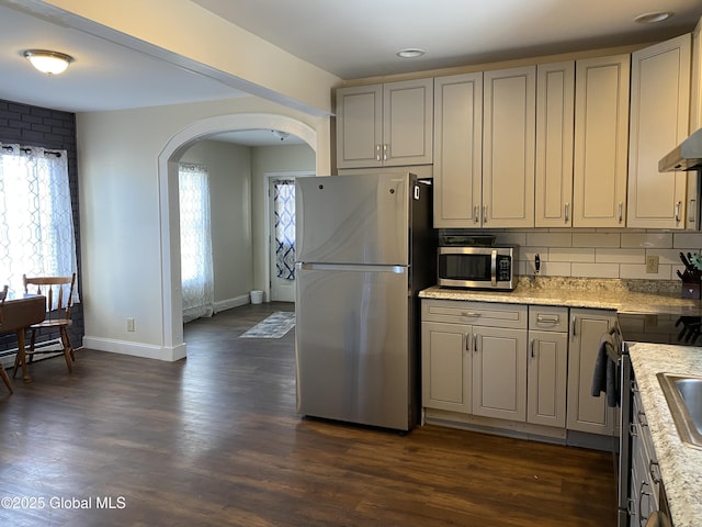 kitchen featuring decorative backsplash, arched walkways, stainless steel appliances, and dark wood finished floors