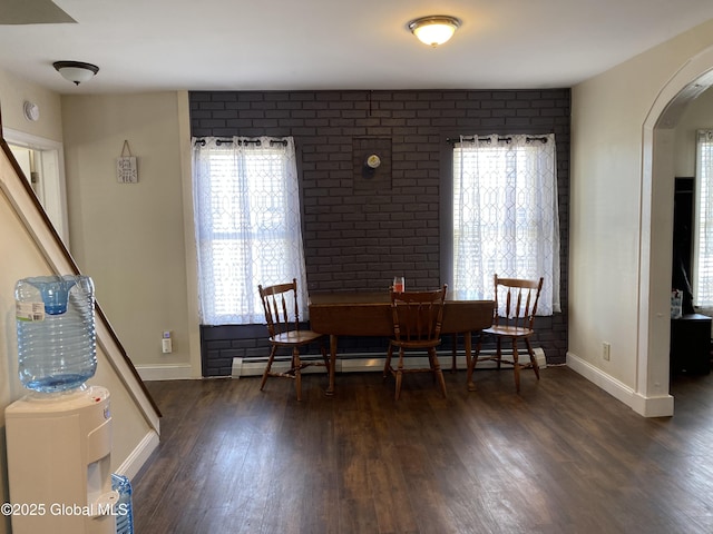 dining room featuring arched walkways, baseboard heating, brick wall, wood finished floors, and baseboards