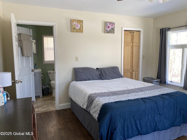 bedroom with a closet, connected bathroom, baseboards, and wood finished floors