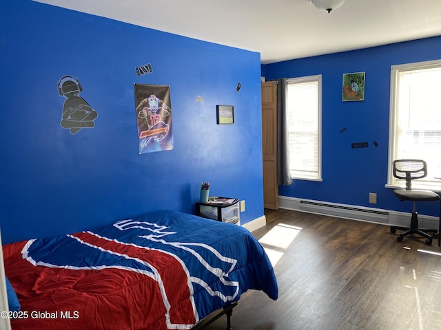 bedroom featuring a baseboard heating unit, multiple windows, baseboards, and wood finished floors