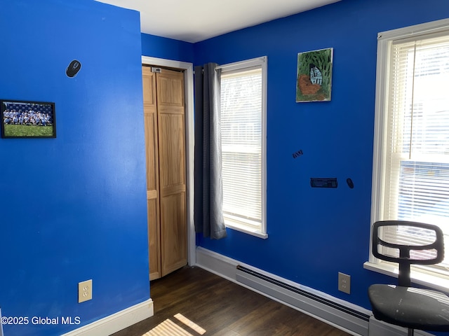 unfurnished bedroom featuring a closet, dark wood-style flooring, a baseboard heating unit, and baseboards