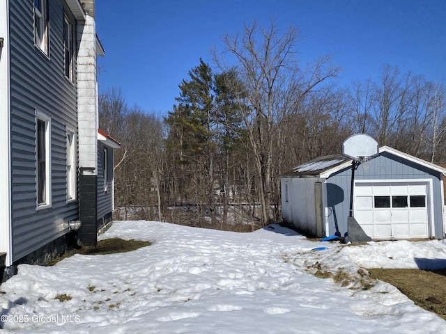 yard layered in snow featuring an outbuilding and a detached garage