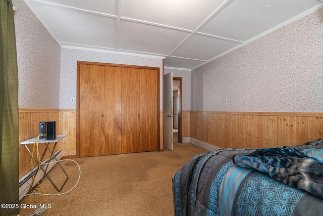 carpeted bedroom featuring wallpapered walls, wainscoting, baseboard heating, crown molding, and a closet