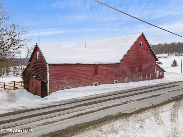 view of snowy exterior with an outbuilding, a barn, a garage, and fence