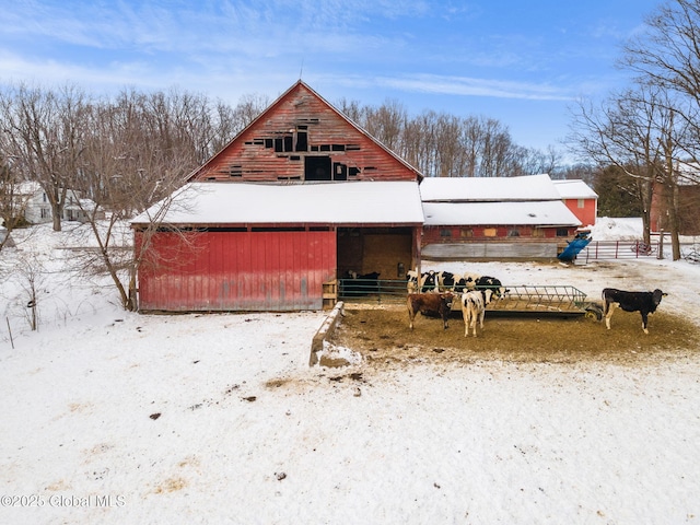 snow covered house with a barn, a detached garage, and an outdoor structure