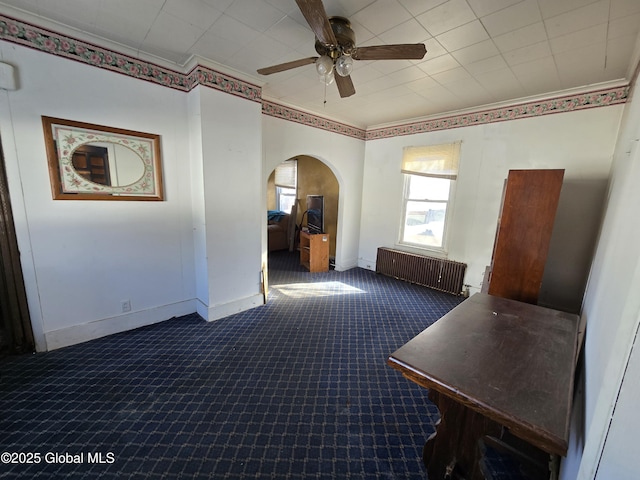 interior space featuring radiator, crown molding, ceiling fan, and dark colored carpet