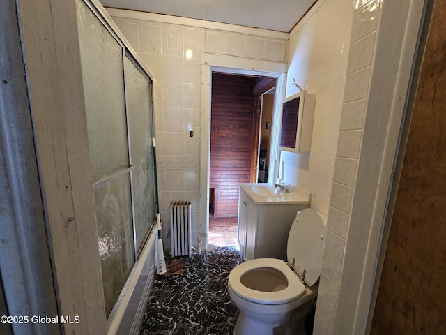 full bathroom featuring combined bath / shower with glass door, radiator, tile walls, vanity, and toilet