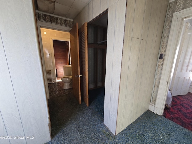 corridor featuring dark colored carpet and wood walls