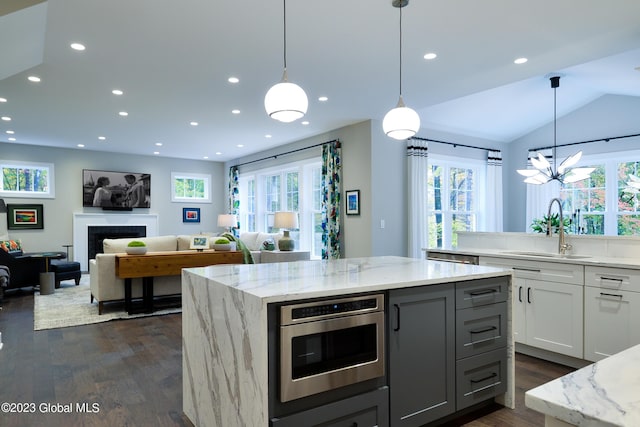 kitchen featuring sink, hanging light fixtures, a center island, light stone countertops, and white cabinets